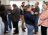 People networking and talking at an indoor business event, standing in small groups in a bright meeting space.