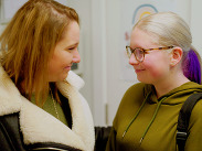 A woman and teenage girl smiling at each other.