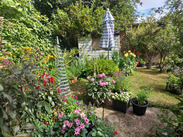 Colourful garden with flowering plants, pots and ornaments arranged around a lawn and shed, showcasing a 2025 Garden competition entry.