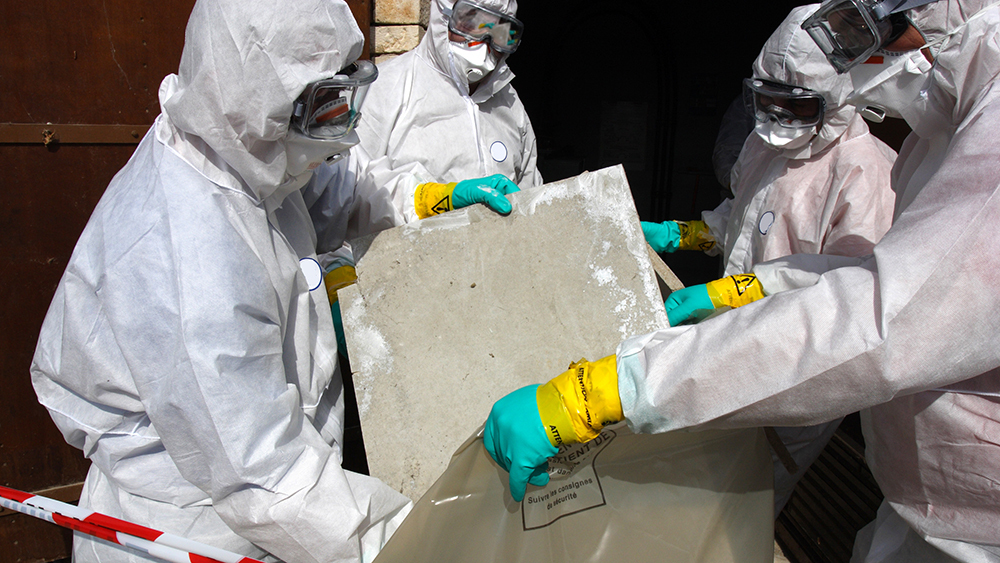 Stock image of staff removing materials containing some asbestos, wearing protective suits and gloves during controlled removal work.