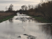 Flooded section of the A361 with standing water covering the road, a white arrow marking visible, and a vehicle stopped in the distance.