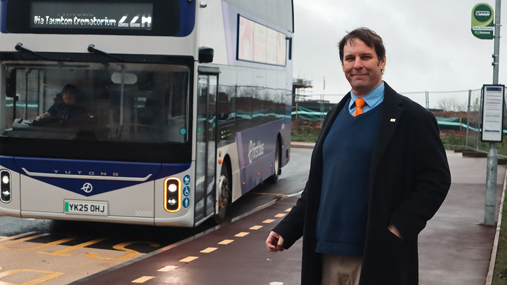 Councillor Richard Wilkins waiting at a bus stop for an approaching bus.