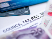 A Council Tax Bill in between Pound Sterling bank notes and bank payment cards.