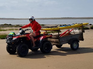 RNLI Lifeguard driving a quad bike along the beach towing rescue equipment during coastal patrol, by Brett Schofield.