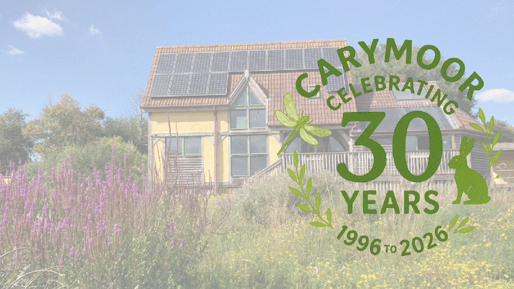 Exterior of a building with solar panels, surrounded by wildflowers, overlaid with text: “Carymoor celebrating 30 years, 1996 to 2026”.