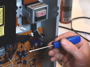 A hand holding a screwdriver repairing a opened DVD player.