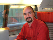 Mark Smith, owner of British travel website The Man in Seat Sixty‑One, seated on a train with notebook.