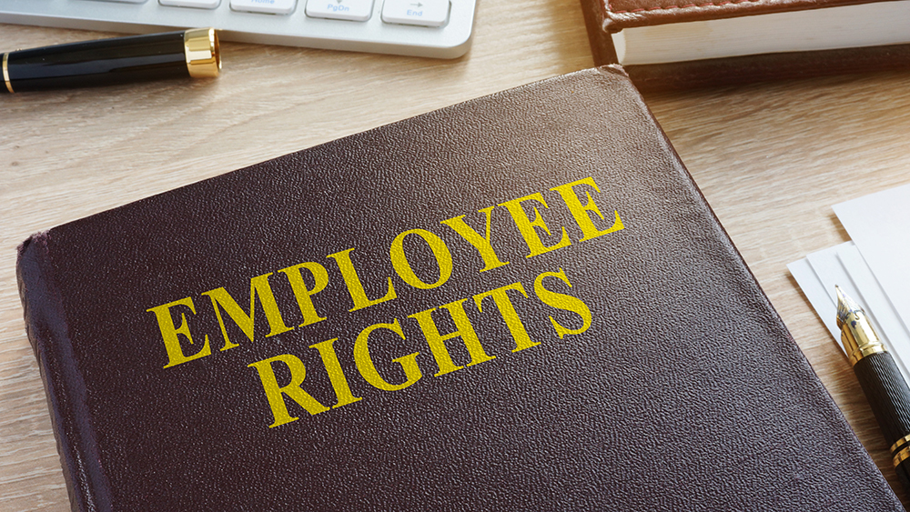 Hardback book titled “Employee Rights” on a desk, alongside a pen, keyboard and papers in an office setting.