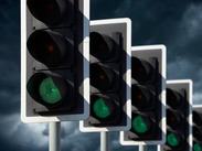 Traffic lights showing green signals in a row against a cloudy sky, indicating traffic flow and road safety controls.
