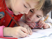 2 young children writing in a book together.