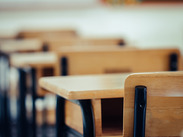 Empty classroom with rows of wooden desks and chairs, photographed close-up with a blurred background.