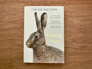 Book cover of Raising Hare by Chloe Dalton, featuring a close-up illustration of a hare against a pale background on a wooden surface.