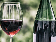 Glass of Wolfblur red wine beside bottle on table with soft green background, suggesting relaxation or social drinking.