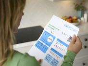 Person holding an energy bill at home, showing charges and payment details on a printed statement with a QR code.
