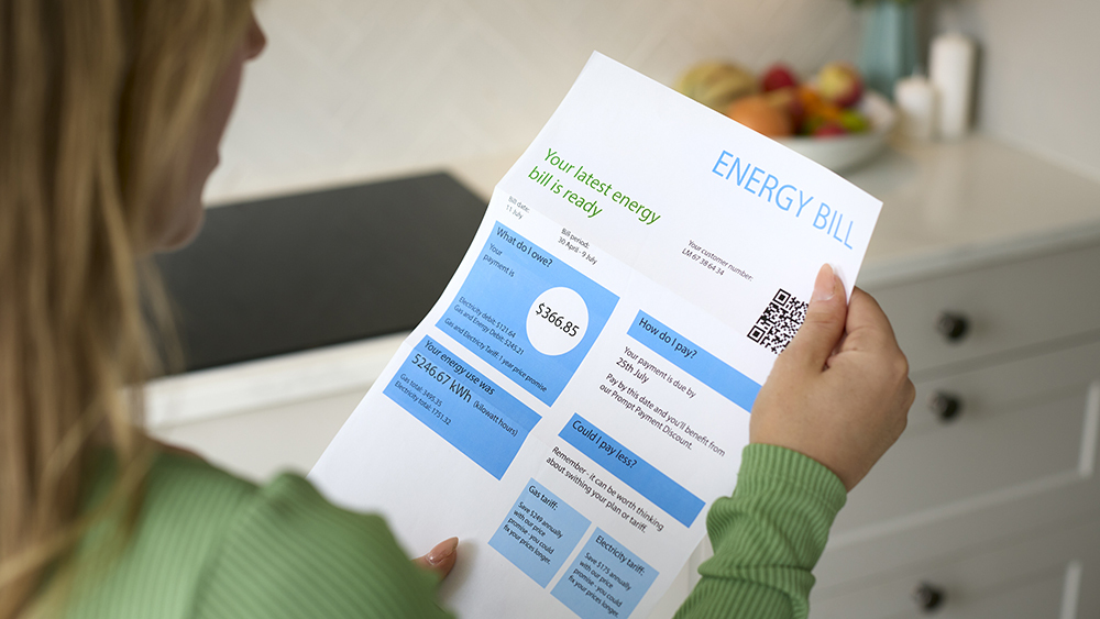 Person holding an energy bill at home, showing charges and payment details on a printed statement with a QR code.