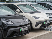 A row of BYD cars are displayed in a showroom forecourt, parked close together with green number plates on a wet surface.