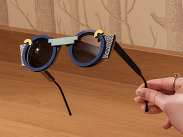 Sustainable glasses by SG Eyecare held above table, bold geometric frames in blue, black and patterned accents.