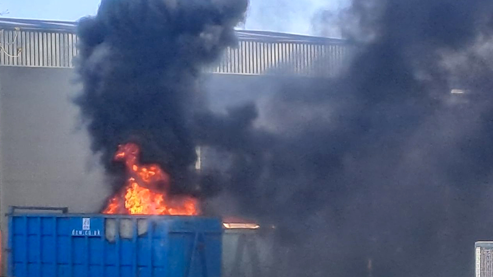 Fire engulfing a blue waste container with thick black smoke rising at a Material Recycling Facility.