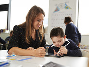 Teacher supports young pupil using a tablet in classroom, illustrating personalised learning and additional education support.