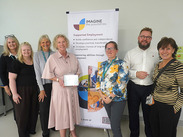 Imagine the Possibilities team holding award plaque at Fiveways School, standing in front of supported employment banner.
