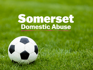 Black and white football on a pitch with Somerset Domestic Abuse logo.