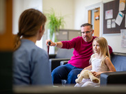 Father and young girl with soft toy speaking to support worker in waiting room during family support or social care meeting.