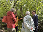 Group discussing outdoors at Carymoor Environmental Centre; Rupert Farthing (right) speaks with visitors among trees and willow fencing.