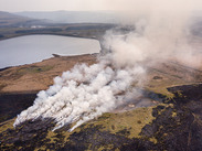 Aerial view of a huge wildfire on moorland near reservoir, with smoke rising over charred ground and surrounding countryside.