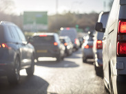 Traffic congestion on a sunlit motorway with cars and vans in slow-moving lanes during bright, hot weather.