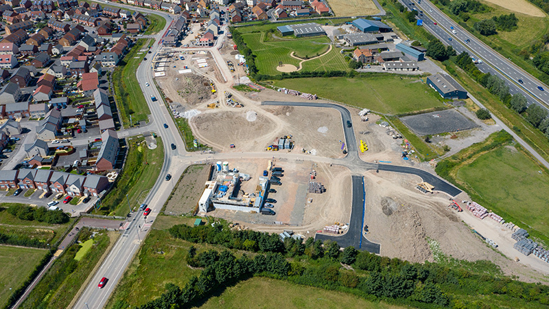 Aerial view of a planning site showing new housing construction, roads and infrastructure next to existing homes and a motorway.