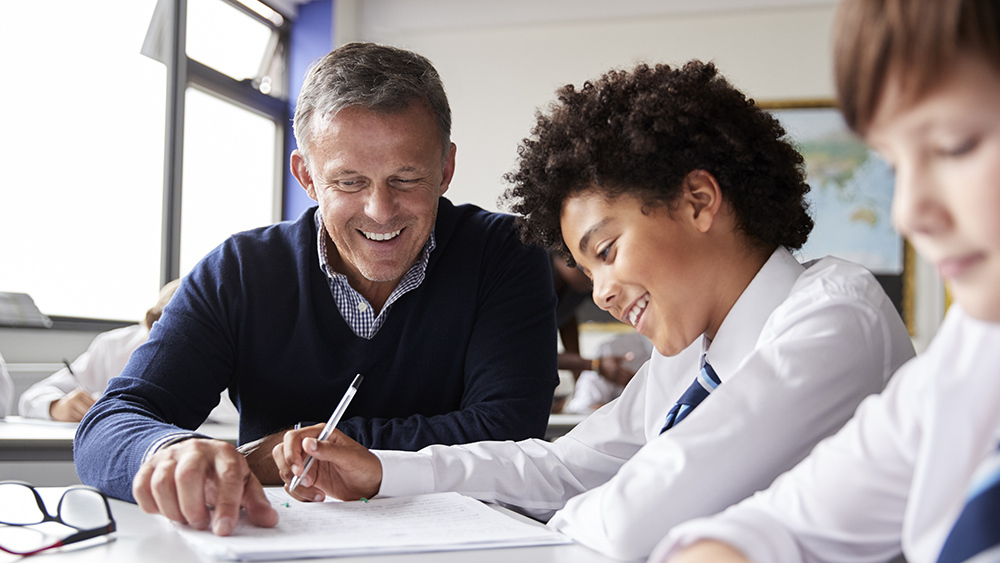 Teacher provides one-to-one support to a pupil in a classroom, helping with schoolwork and learning development.