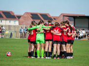 Group of girls on a football pitch in a huddle in a football game by Somerset FA.