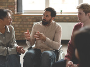 Man in a wheelchair gesturing and engaging in discussion with others during a supportive group.
