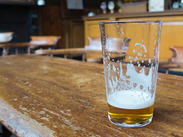 Nearly empty pint glass with a small amount of beer and foam residue, resting on a wooden pub table.