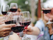 People raising glasses of red wine in a social setting, making a toast together outdoors.