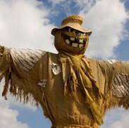 Traditional scarecrow made from hessian fabric and straw, with outstretched arms, a straw hat and a painted face.