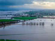 Aerial view of flooding across fields in the Moorland area, with waterlogged farmland, scattered trees and distant villages under cloudy skies.