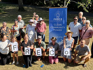 Members of Frome Renewable Energy Co-op gather outdoors beside a FRECO banner, holding letters that spell FRECO.