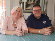Heather and Paul sit at a dining table in their home, smiling as they share their foster caring story in Somerset.