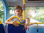 Two children travelling on a bus, looking out towards the road ahead from the front seating area.