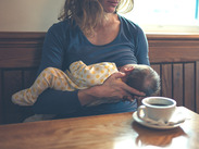 A young mother breastfeeding her baby in a café whilst having a coffee.