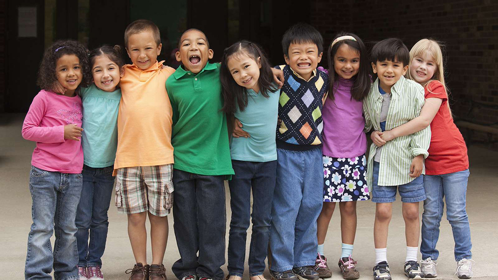 Group of eight primary school-aged children standing arm in arm outside a school building.