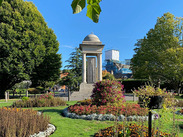 War Memorial in Vivary Park, Taunton, surrounded by colourful flower beds, lawns and mature trees on a sunny day.