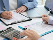 Finance professionals reviewing accounts, audit reports and budget figures around a desk with a laptop and calculator.