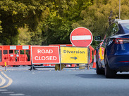 Traffic signs diverting a blue car around fenced-off road works.