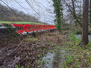 Temporary safety barriers line the collapsed riverside wall beside the River Sheppey near Croscombe.