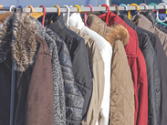 A row of winter jackets, including brown, white, red, and blue colours, hanging on a metal rack outdoors.