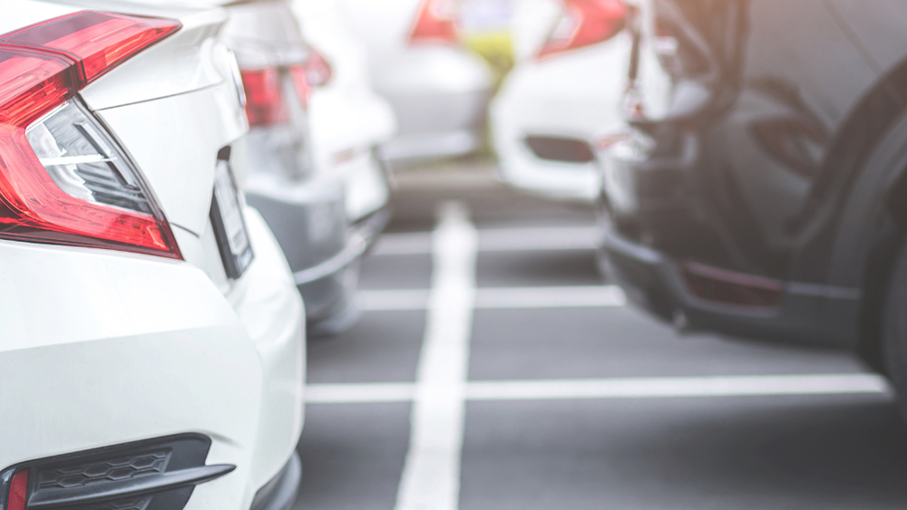 Cars parked in marked parking bays, showing the rear ends of several vehicles in a car park with shallow depth of field.