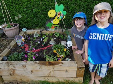 2 children standing next to a fairy garden they have made