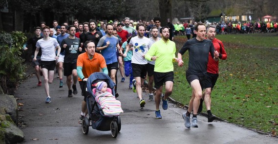 A group of runners with a man pushing a pushchair at the front